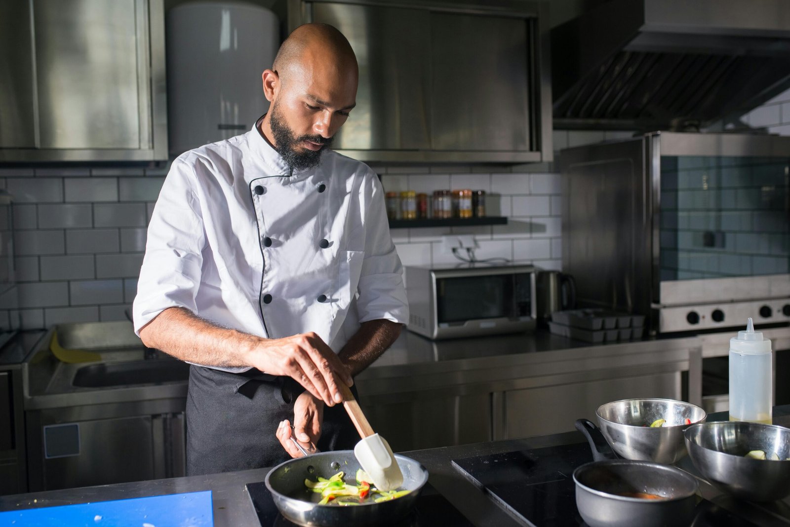 A skilled chef prepares fresh vegetables in a frying pan in a well-equipped kitchen.